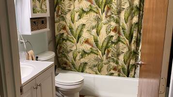 Ein Badezimmer mit Toilette, Waschbecken und Badewanne. Ein Duschvorhang mit tropischem Blattmuster.