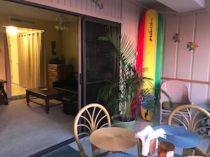 A cozy room with a glass table, wicker chairs, a potted plant, and a surfboard decoration.
