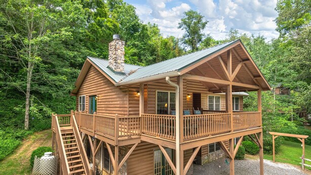 Une cabane en bois dotée d’un balcon et d’une cheminée en pierre, entourée d’arbres.