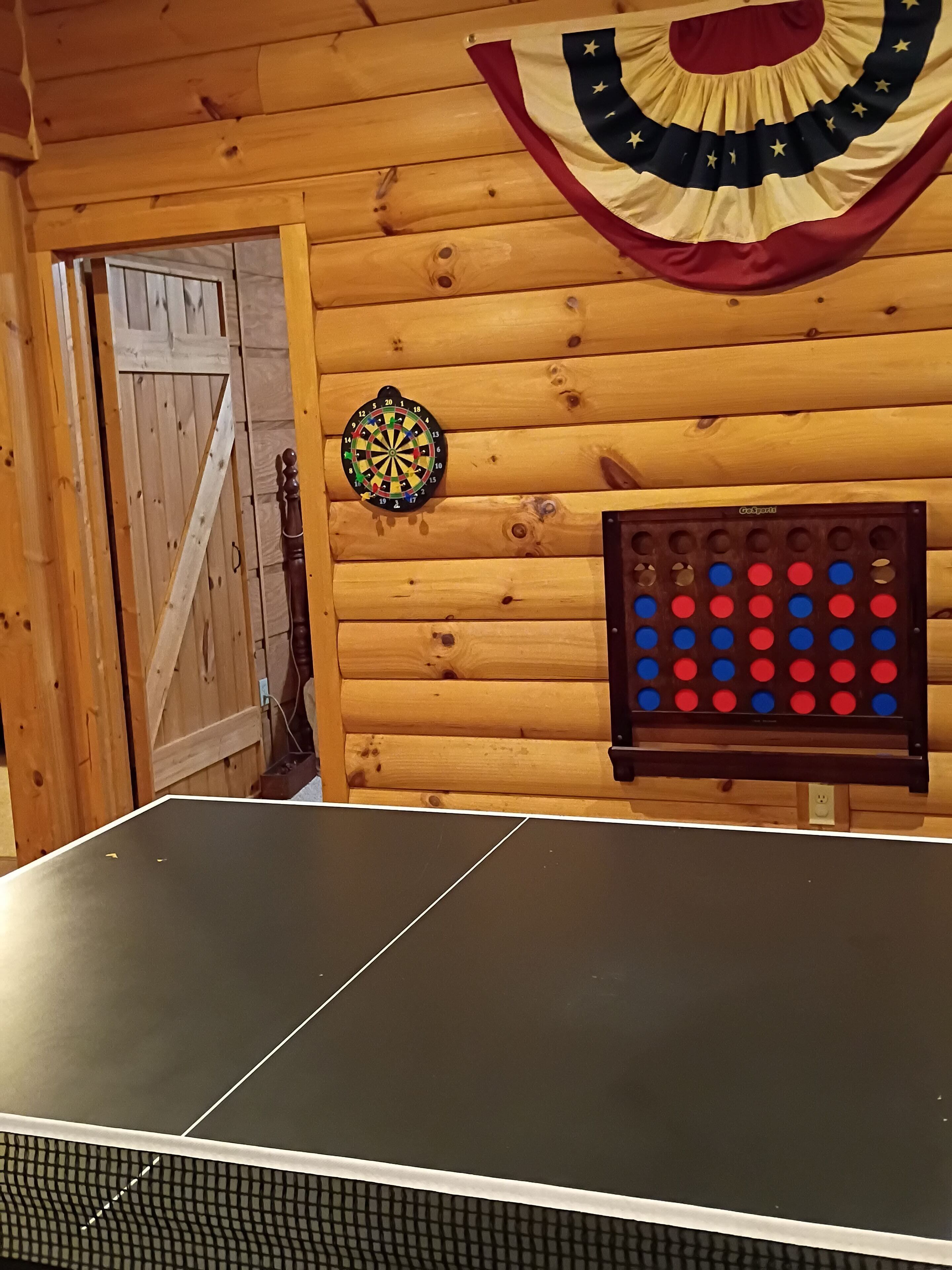 A ping pong table in a room with wooden walls, a dartboard, and a game board.