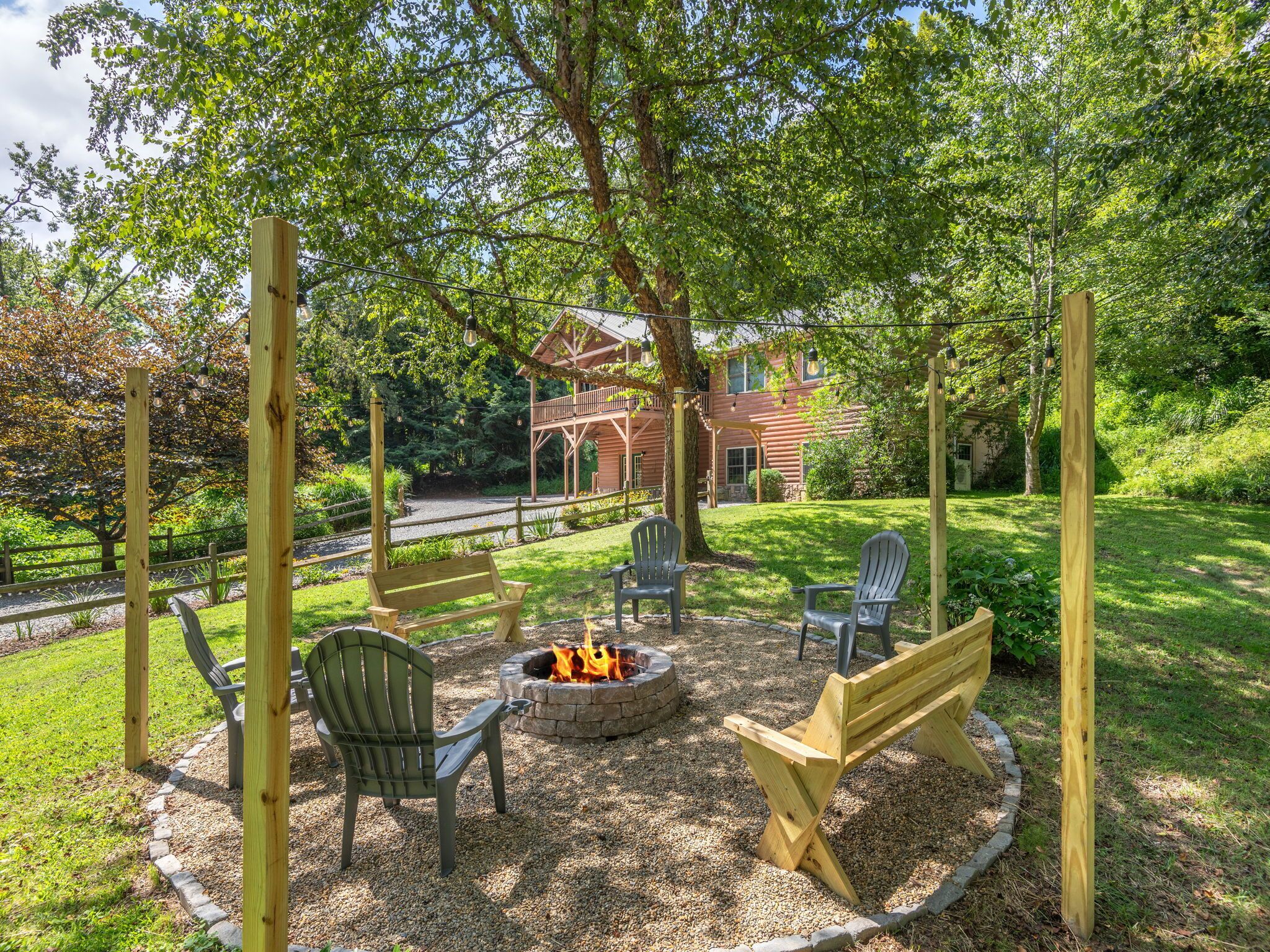 An outdoor seating area with Adirondack chairs and a fire pit, surrounded by a wooden pergola and a grassy lawn.