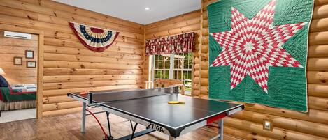 A ping pong table in a room with wooden walls and a large quilt.