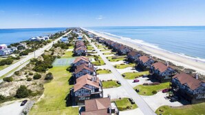 A coastal residential area with houses aligned along a beachfront, featuring a tennis court and a clear view of the ocean. - Spectacular Direct Oceanfront 2BR Condo in Emerald Isle NC Ocean Reef 7B1 (Emerald Isle)