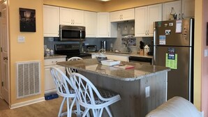 A kitchen with white cabinets, a central island with bar stools, a microwave, stove, and refrigerator. - Spectacular Direct Oceanfront 2BR Condo in Emerald Isle NC Ocean Reef 7B1 (Emerald Isle)