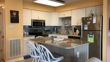 A kitchen with white cabinets, a central island with bar stools, a microwave, stove, and refrigerator.