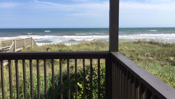 A wooden deck overlooking a beach with waves crashing onto the shore. - Spectacular Direct Oceanfront 2BR Condo in Emerald Isle NC Ocean Reef 7B1 (Emerald Isle)