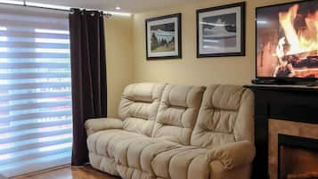 A living room with a beige sofa, a fireplace, and two framed pictures on the wall.