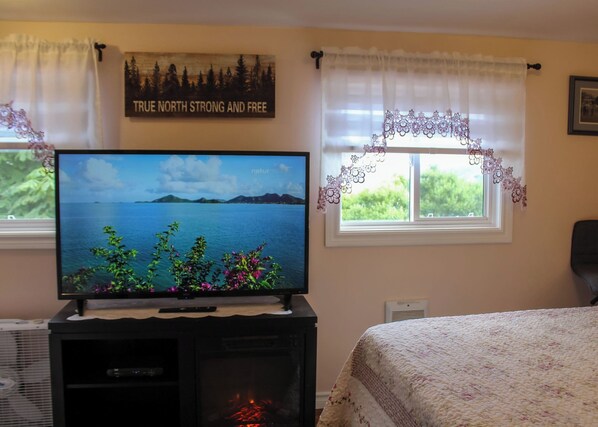 A television on a stand, a window with a view of greenery, and a wall with a 'True North Strong and Free' sign.