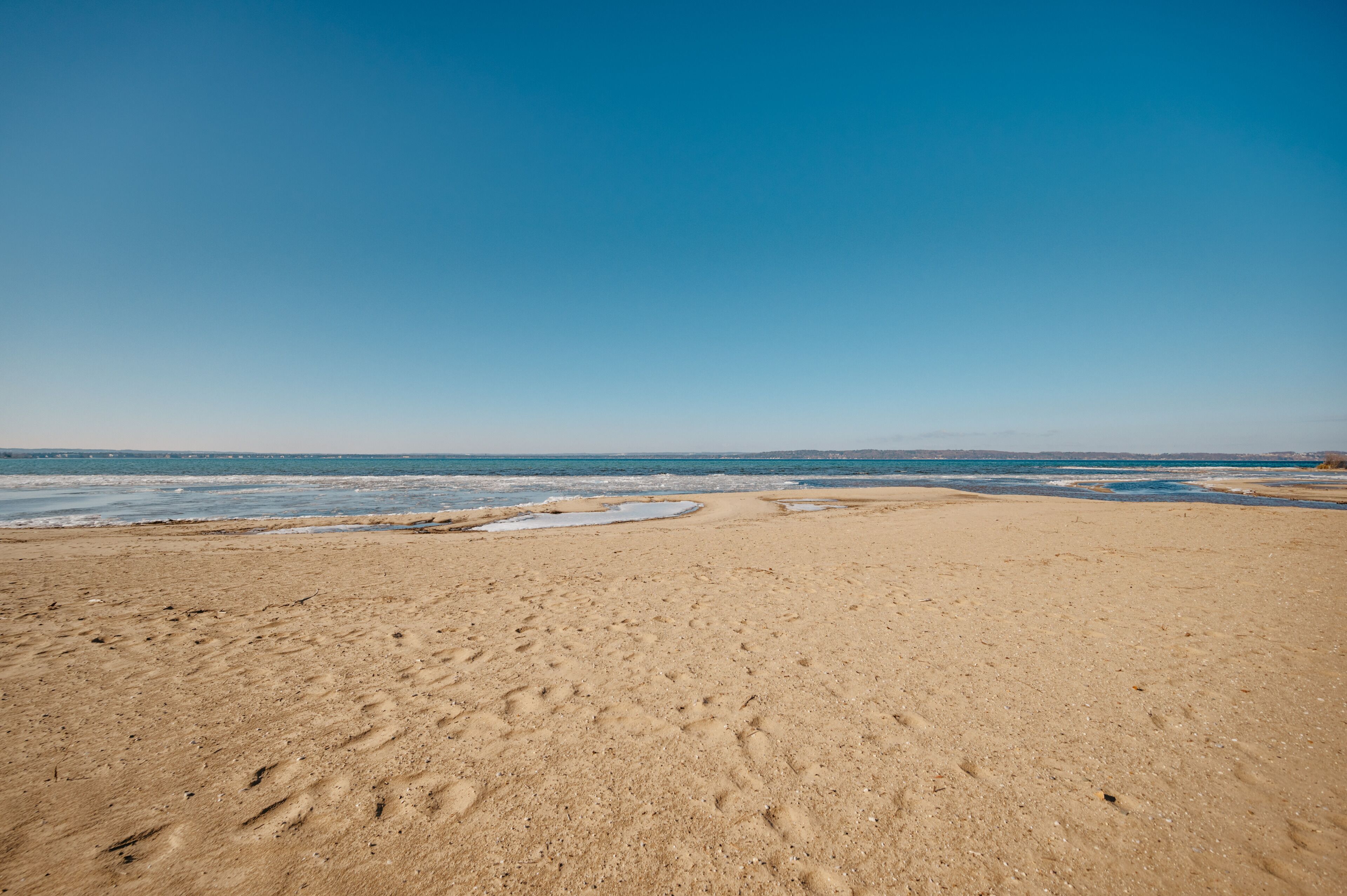 Ein sandiger Strand mit Fußspuren, die zum Wasser führen.