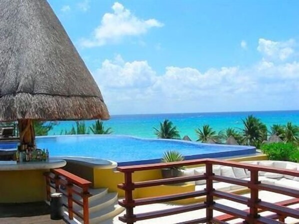 A poolside area with a thatched roof, a bar, and a view of the ocean.