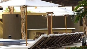 A row of sun loungers under a white umbrella, a pool, and a building with a yellow facade. - Fab Condo - 14 Steps to Beach, with Panoramic Roof View (Playa del Carmen)