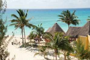 A beach with thatched-roof huts, palm trees, and a clear view of the ocean.