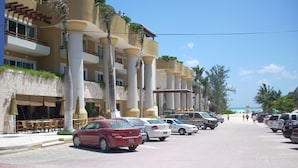 A hotel with multiple floors, outdoor seating, and parked cars along the street. - Fab Condo - 14 Steps to Beach, with Panoramic Roof View (Playa del Carmen)