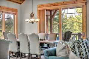 A dining area with a wooden table, upholstered chairs, and a hanging light fixture. - Sierra Sanctuary | Mountain Views with Club and Golf Access! (Truckee)