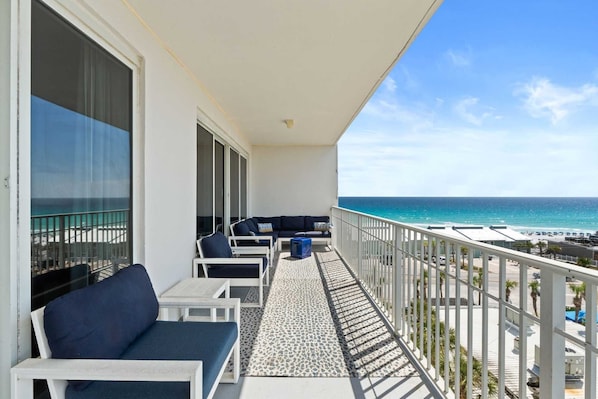A balcony with a sofa and chairs, a view of the ocean, and a railing.