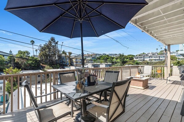Een terras met buitenmeubilair, waaronder een tafel en stoelen, onder een grote parasol.