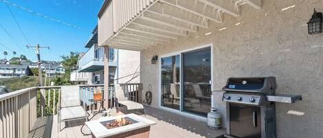 A covered deck with a grill, a fire pit, outdoor furniture, and a view of neighboring buildings.