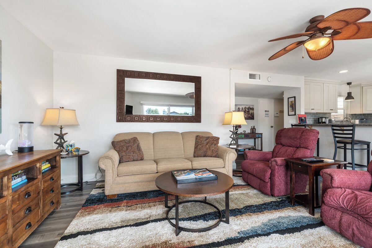 A living room with a beige sofa, a red armchair, a coffee table, and a ceiling fan.