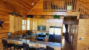 A wooden cabin with a kitchen featuring granite countertops, a central island with bar stools, stainless steel appliances, and a wooden balcony. - Near Wine Country & Parks. Great Hiking & Amazing Views! Reduced June rates! (Hays)