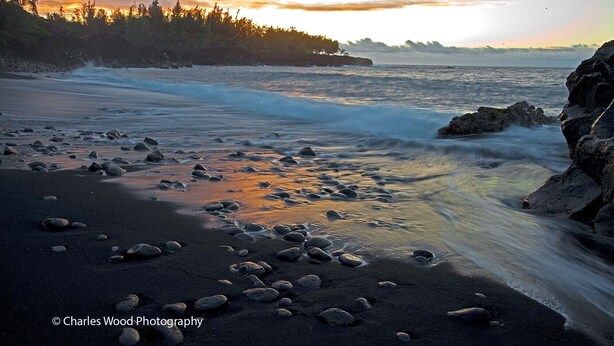 Ein Strand mit Felsen und Wellen bei Sonnenuntergang.