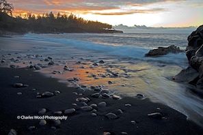 Enjoy the tranquil beach scene with gentle waves lapping at the shore and a forested backdrop.