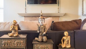 Ein Wohnzimmer mit einer Couch, einem an der Wand montierten Fernseher und dekorativen Statuen auf Beistelltischen.