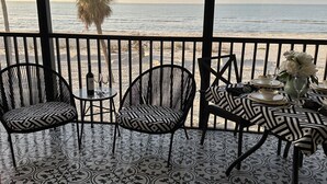 A balcony with a view of the ocean, featuring patterned floor tiles, black and white chairs, and a table set for dining. - E25 Direct Gulf Front is open!  Beautiful and new!  Saturday-Saturday (Sanibel)