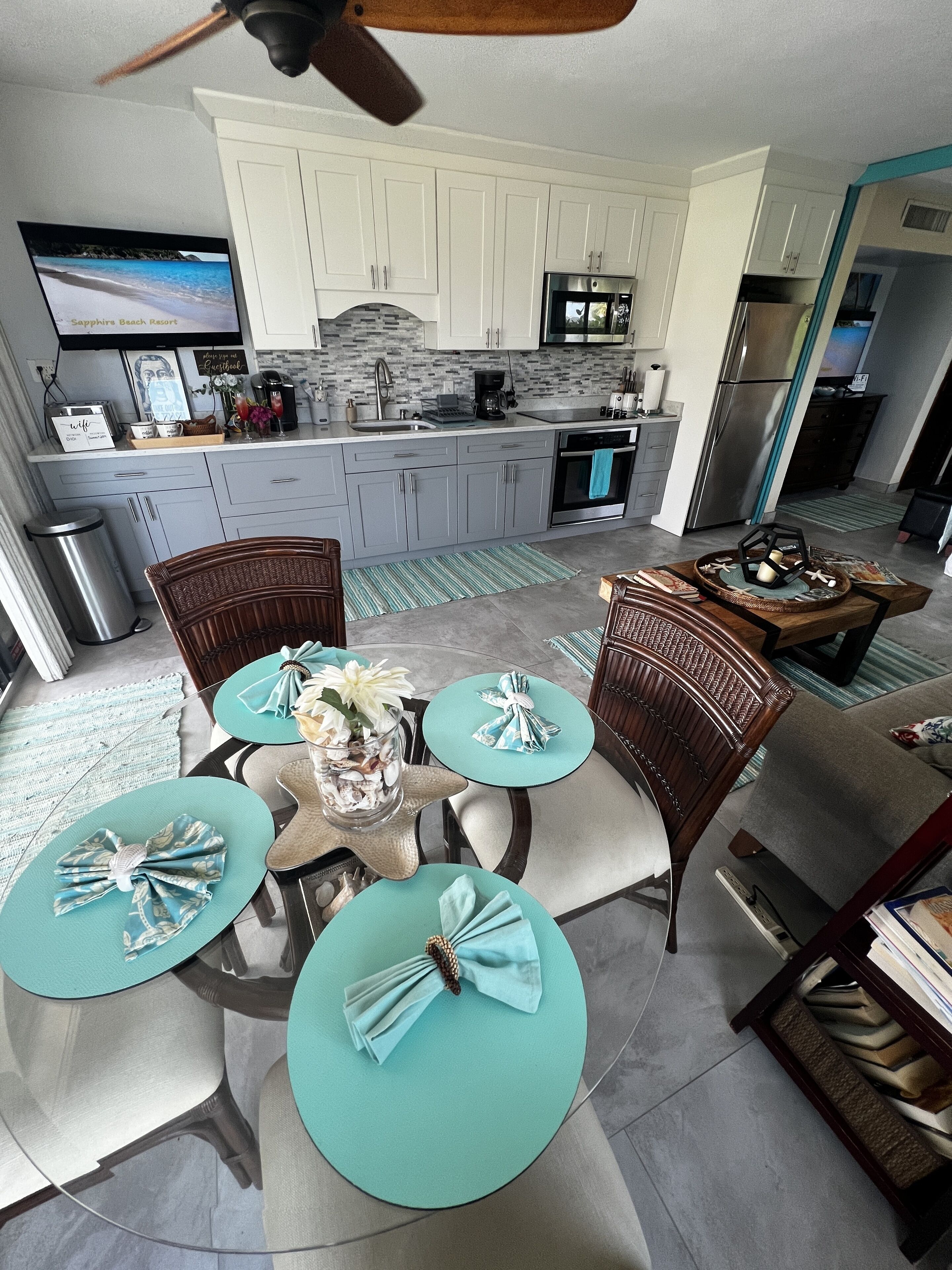 A modern kitchen with white cabinets, a stainless steel refrigerator, and a flat-screen TV mounted above the counter.