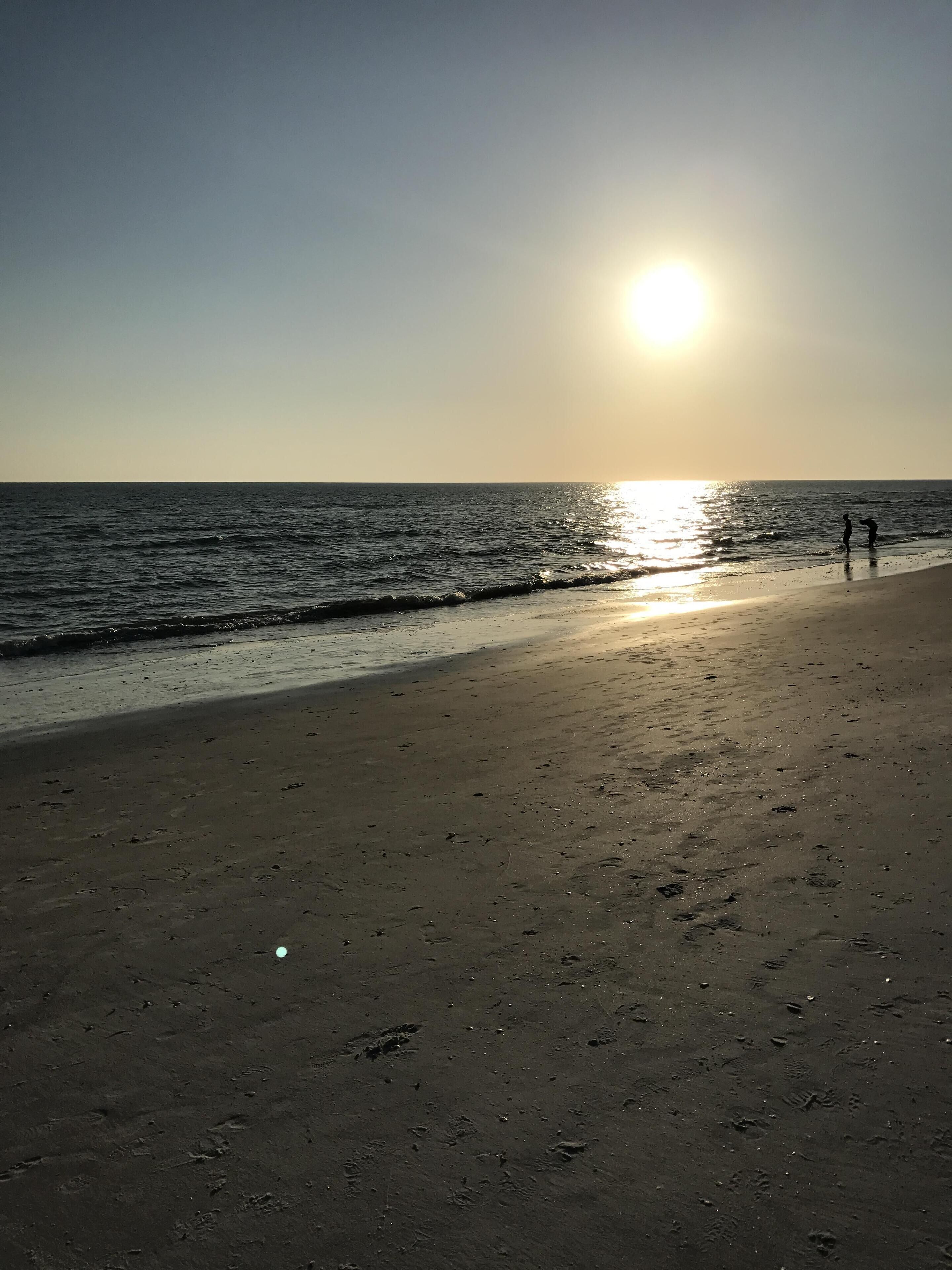 Een strand met de ondergaande zon boven de oceaan.