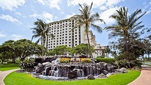 A hotel with a central water feature surrounded by well-maintained grass and palm trees.