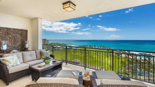 A balcony with a view of the ocean, wicker furniture, and a decorative wall.