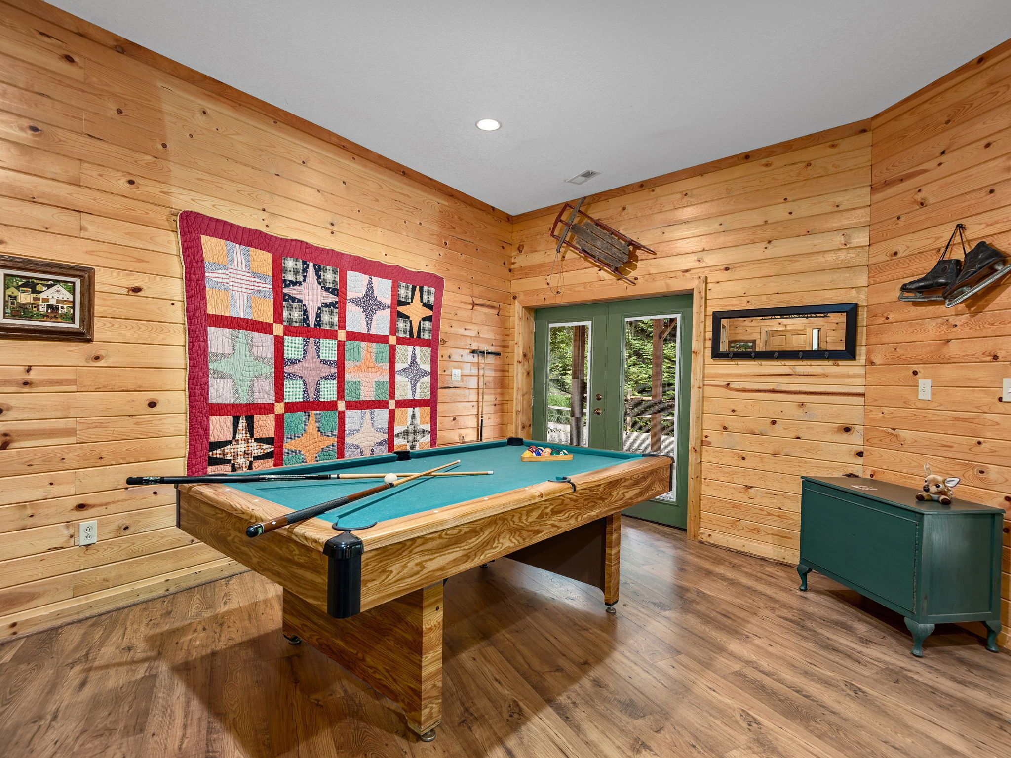 Une table de billard dans une pièce en bois avec une porte verte, un petit meuble et un tableau encadré au mur.