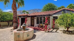 Una casa con tetto in tegole, un patio con mobili da esterno e un giardino con una palma e fiori.