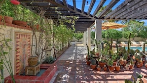 Un patio coperto con piante in vaso, un vialetto piastrellato e una piscina sullo sfondo.