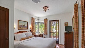 Una camera da letto con un letto grande, un quadro appeso al muro, una scrivania con un televisore e una finestra con tende.