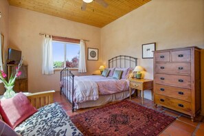 A bedroom with a bed, bedside tables, a dresser, a television, and a window with curtains.