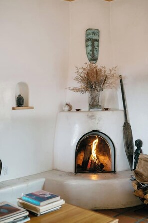 A cozy room with a fireplace, a shelf with decorative items, and a table with books.