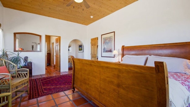 A bedroom with a wooden bed, a red rug, and a ceiling fan.