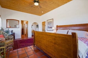 Un dormitorio con cama de madera, un tapete rojo y un ventilador de techo.