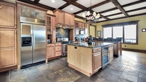 A spacious kitchen with wooden cabinets, a stainless steel refrigerator, a large island, and a stone tile floor. - Multi-Million Dollar Mountain Estate-FOUR STATE VIEWS (Banner Elk)