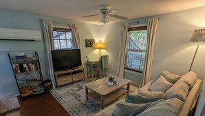 Una sala de estar con sofá, televisor, estantería y ventilador de techo.