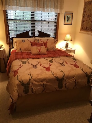 Relax in a serene bedroom with a large bed, deer-themed quilt, and a bedside table with a lamp.