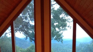 A room with large windows offering a view of a forested mountain range. There are signs on the windows that read "IMAGINE" and "BE OUR GUEST".