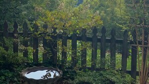 A view of a mountainous landscape with a wooden fence and a birdbath in the foreground.