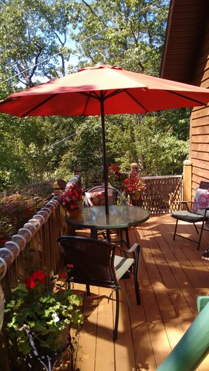 Relax on the patio with a round table and two comfortable chairs, surrounded by lush greenery and a charming wooden fence.