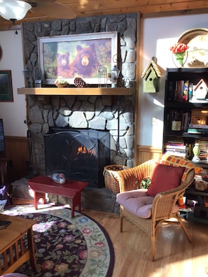 Ein gemütliches Wohnzimmer mit Kamin aus Stein, einer Bücherwand und einem Korbsessel.