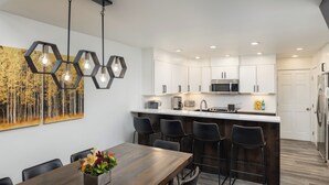 A modern kitchen with white cabinets, a central island, bar stools, and a dining table with chairs. - Enzian 315 - 4 Bedroom Diamond (Vail)