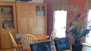 A dining area with a wooden table and chairs, a cabinet with glass doors, and a potted plant.