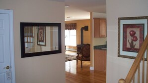 A hallway with a wooden floor, a door with a sign, a framed picture, a chair, and a staircase.
