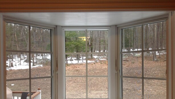 A bay window with a view of a wooded area with snow patches.